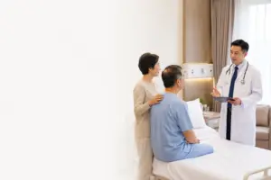 Patient seated calmly in a hospital ward while a urologist explains robotic prostatectomy before surgery, with a family member providing support.